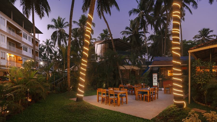Garden dining area at Richmonde Ananta Elite, Goa offering an evening view of the lush outdoor space surrounded by palm trees.