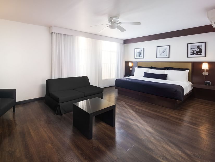 A wide-angle shot of our room in Montego Bay with a large bed, a couch, a wall-mounted televisions and white curtains covering the floor-to-wall windows - S Hotel Kingston, Jamaica