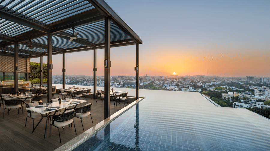Rooftop dining area at The Residency Towers Chennai with an infinity pool and city views during sunset.