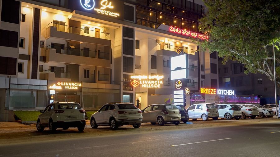 Night view of the hotel exterior with parked cars and lit-up signs along the street at TGI Livancia Hillside, JC Nagar, Mysore