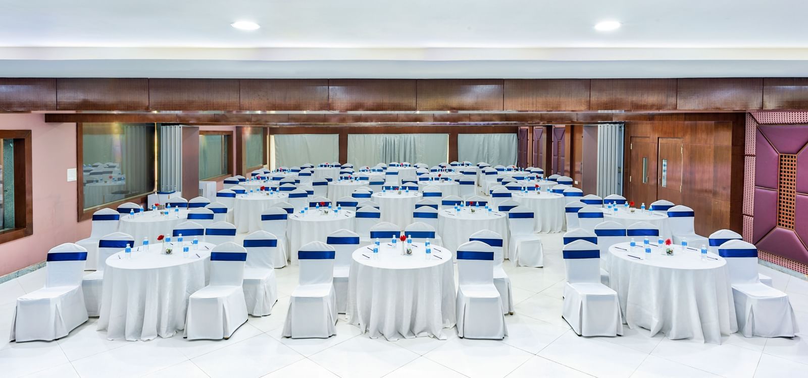Spacious banquet hall with round tables covered in white cloth and blue chairs at Grande Bay Resort & Spa.