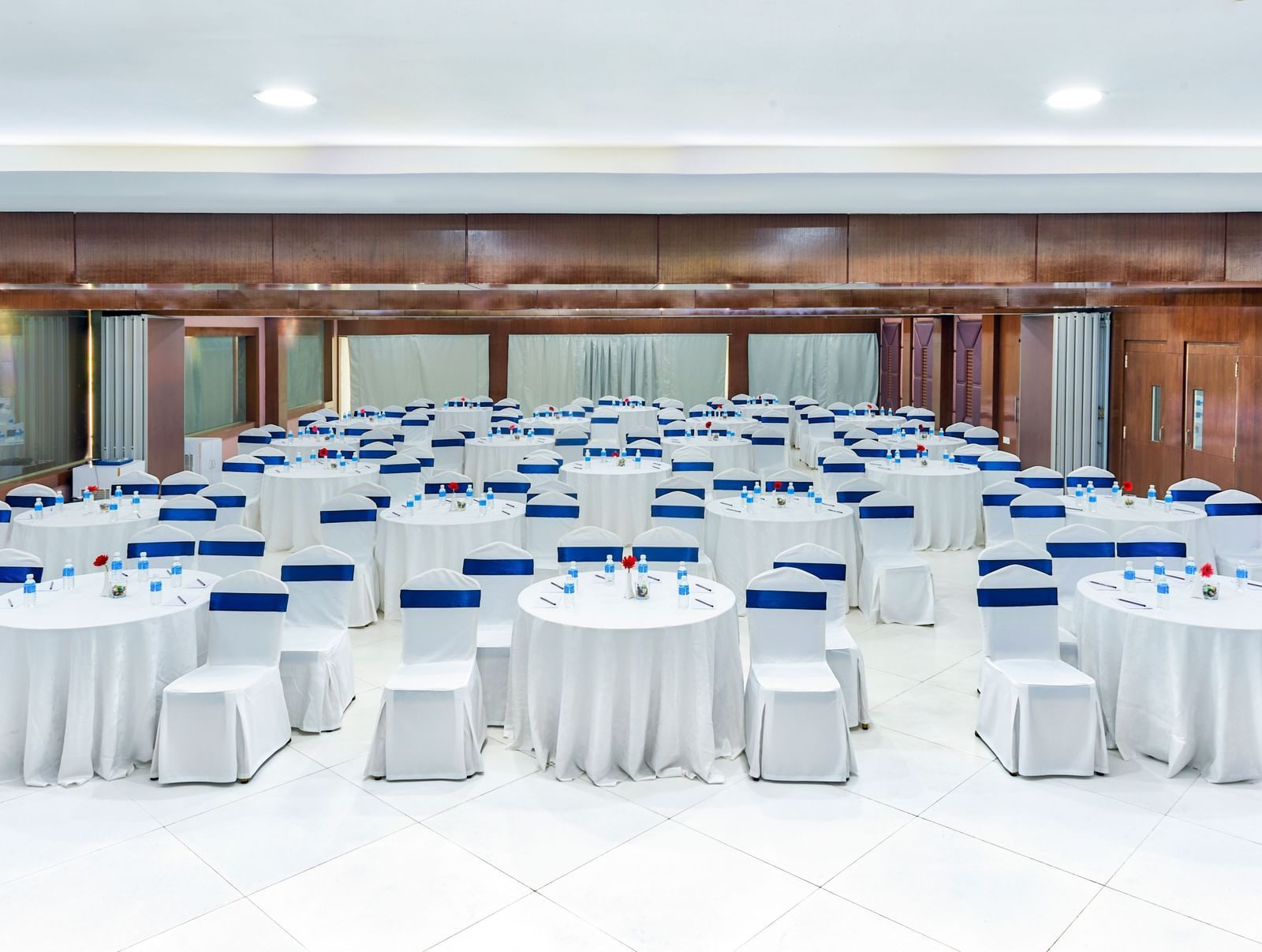 Spacious banquet hall with round tables covered in white cloth and blue chairs at Grande Bay Resort & Spa.