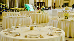 A beautifully arranged banquet hall with round tables covered in white linens and decorated with glassware.