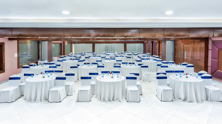 The Pacific Ocean banquet hall arranged with round tables covered in white linen and blue chair covers - Grande Bay Resort & Spa, Mamallapuram