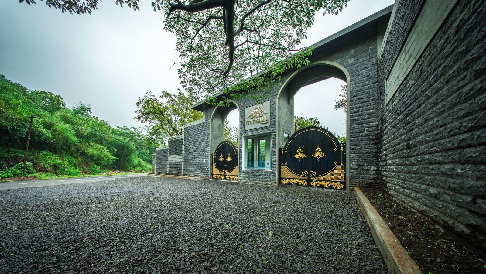 A stone gateway entrance with an arched top with lush greenery around - Tranquil Piedmont Estates & Resort, Lonavala