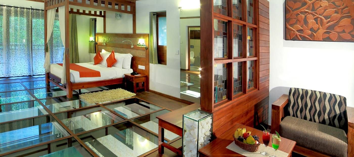 A bed in a room that has glass-flooring along with other wooden furnishings | Vythiri Resort. Wayanad