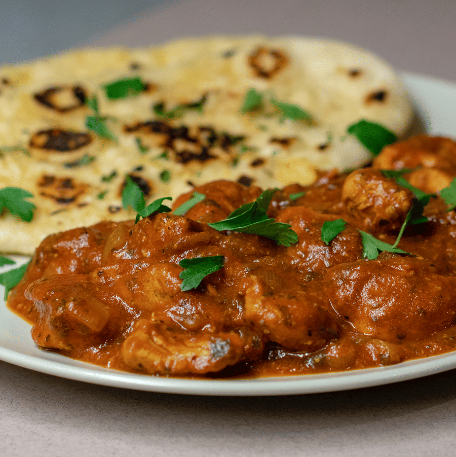 A white ceramic plate served with naan and chicken.
