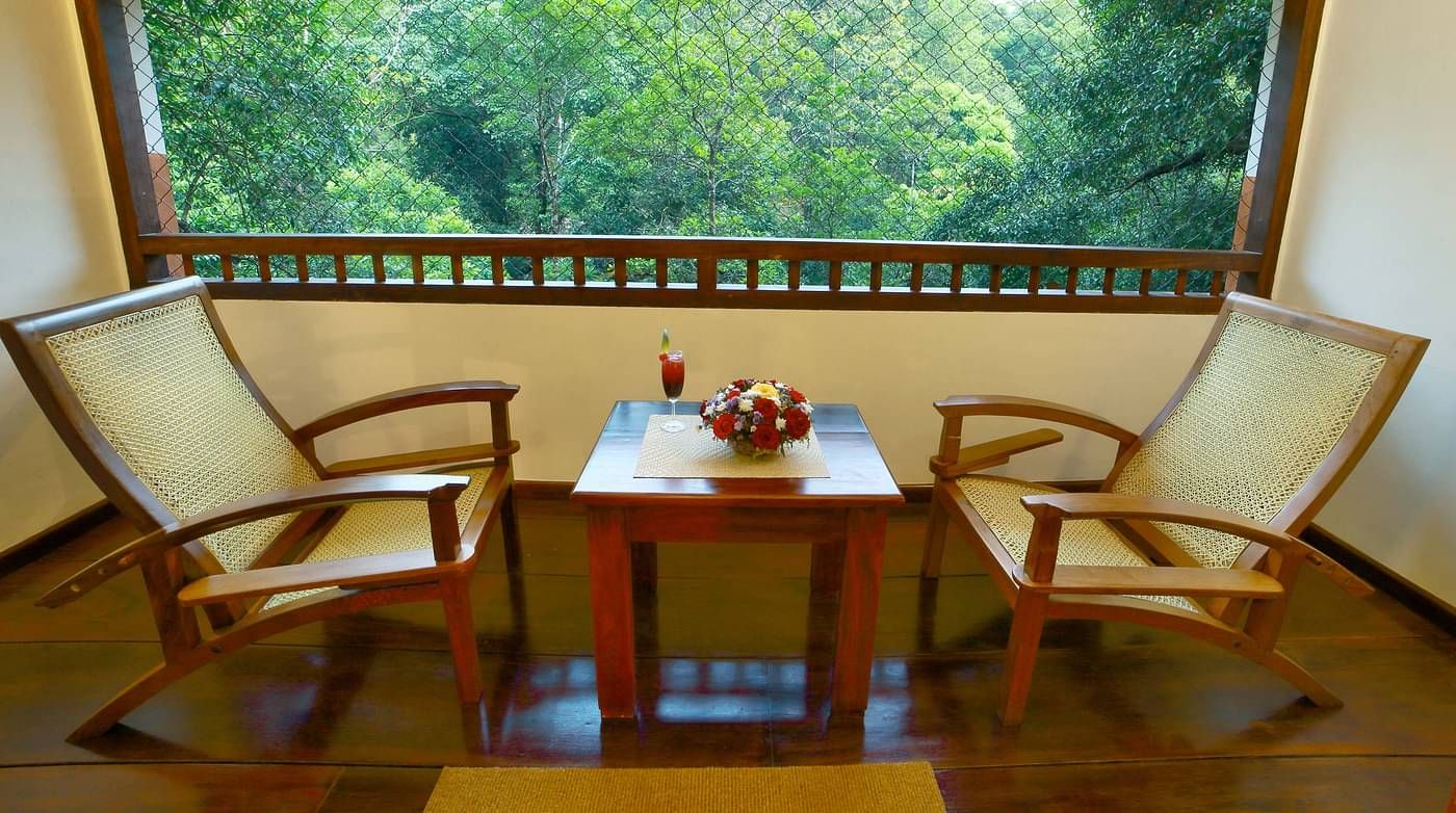 A side view of two chairs placed in a balcony with forest views | Vythiri Resort. Wayanad