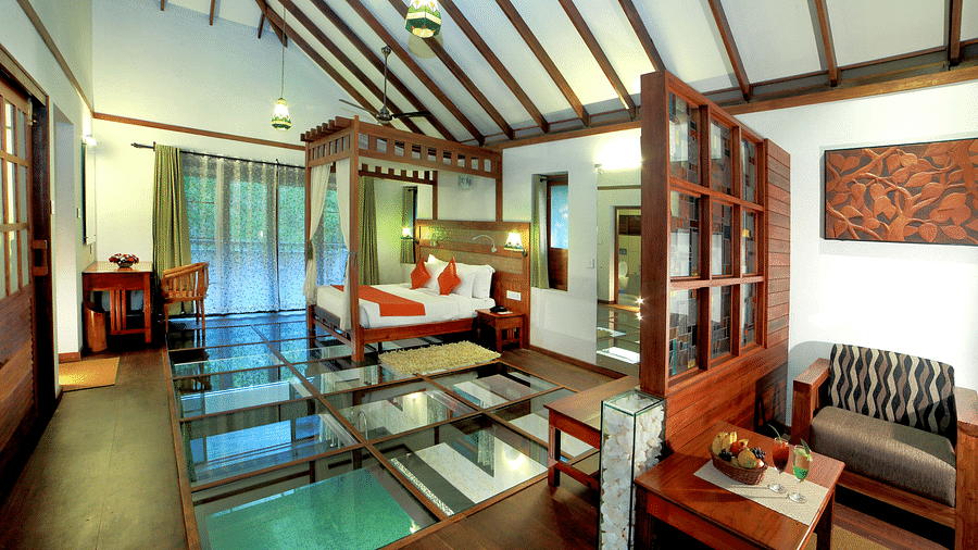 A full view of a glass-floored room that has a bed and other wooden furnishings | Vythiri Resort. Wayanad