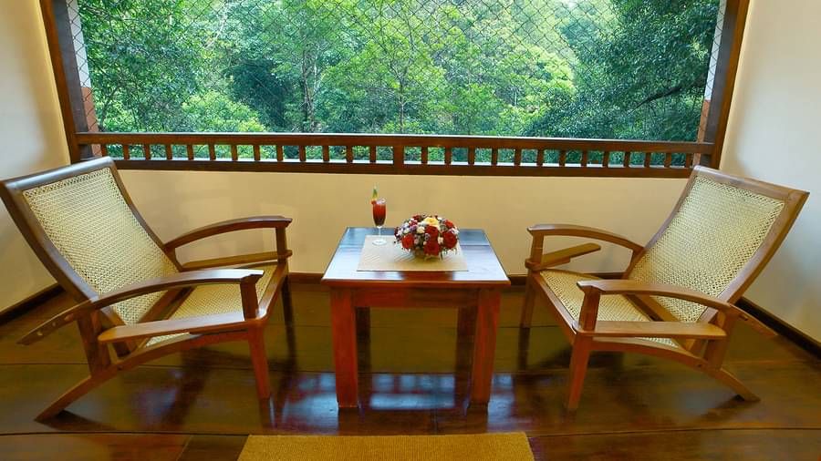 A side view of two chairs placed in a balcony with forest views | Vythiri Resort. Wayanad