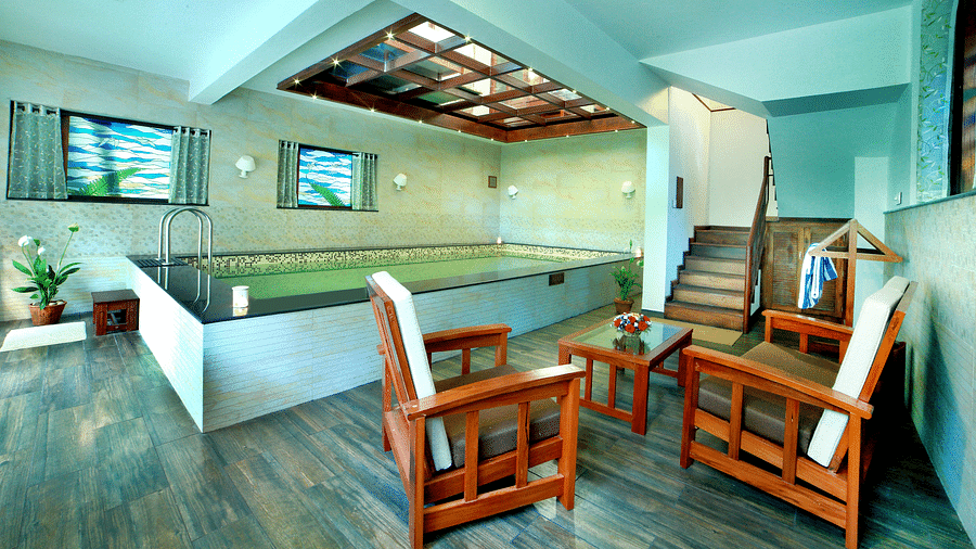 A full view of a pool in a closed space with some chairs on the side | Vythiri Resort. Wayanad
