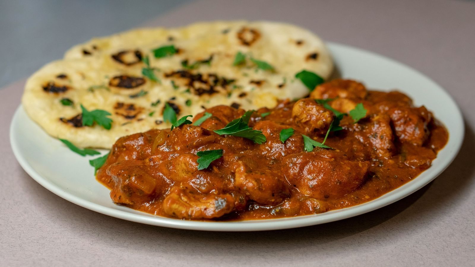 A plate of butter chicken with butter naan on the side kept on the table