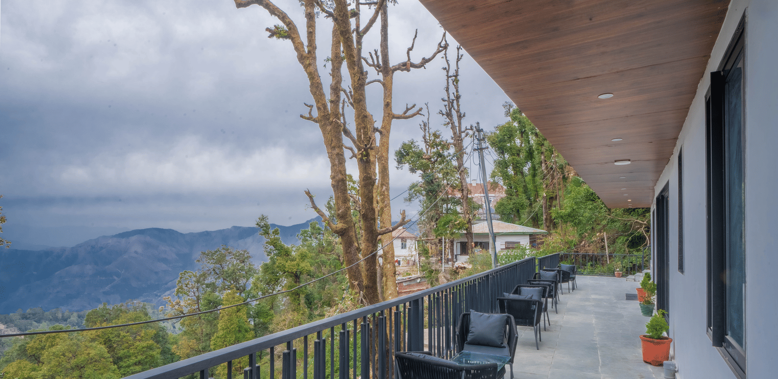 A wide-angle shot of the common balcony for the Deluxe Rooms With Shared Balcony & Valley View featuring several seating spaces overlooking the valley views at Perfectstayz Premium Westend Mall Road, Mussoorie.