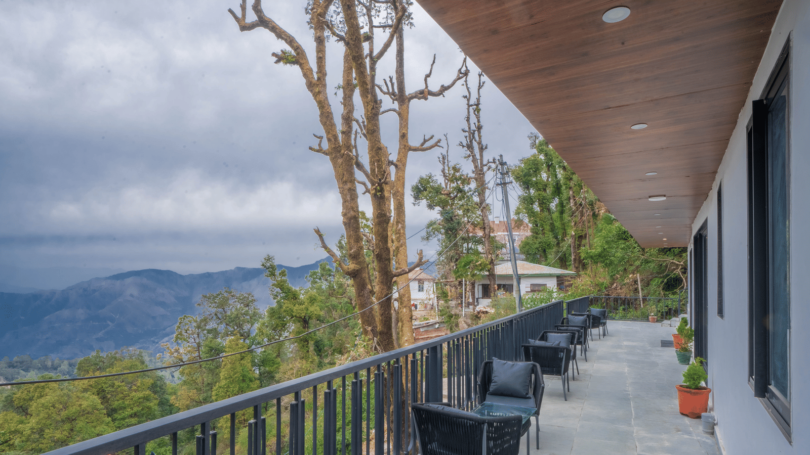 A wide-angle shot of the common balcony for the Deluxe Rooms With Shared Balcony & Valley View featuring several seating spaces overlooking the valley views at Perfectstayz Premium Westend Mall Road, Mussoorie.