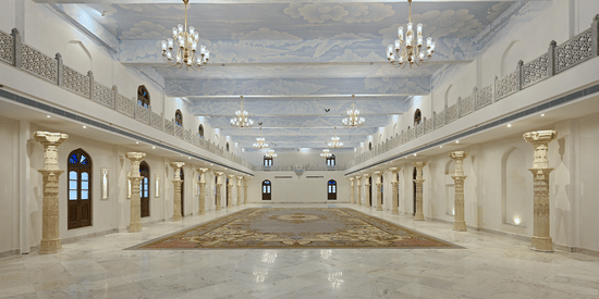 The illuminated banquet hall featuring white and cream decor with numerous chandeliers at Fateh Vilas, a wedding resort in Udaipur