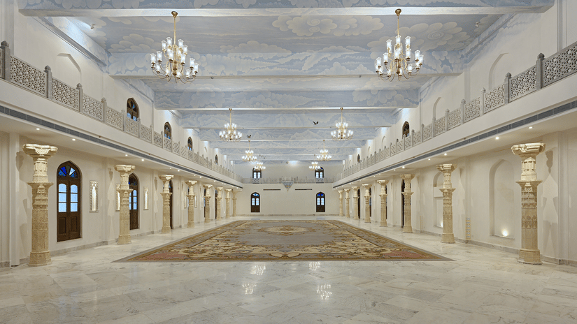 The illuminated banquet hall featuring white and cream decor with numerous chandeliers at Fateh Vilas, a wedding resort in Udaipur
