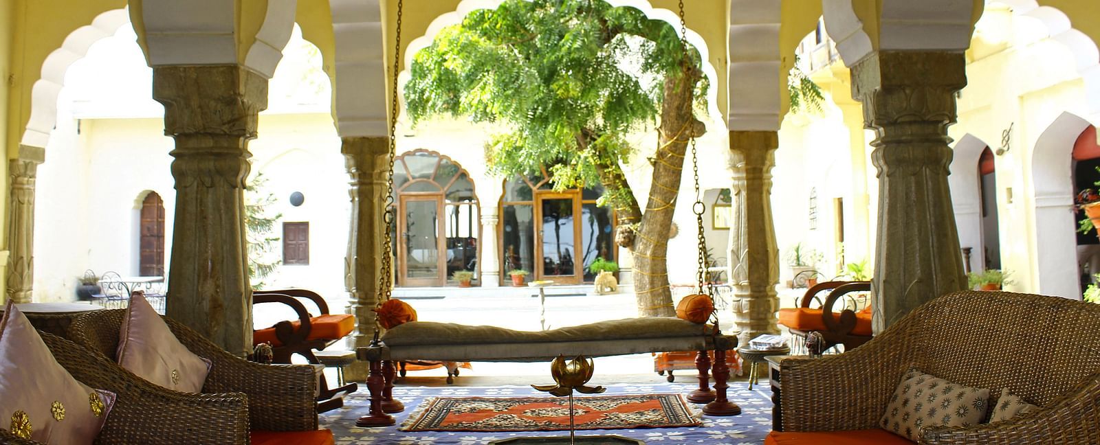 An inviting courtyard lounge at Fort Barli, with plush seating framed by arched columns, opens onto a lush garden view.