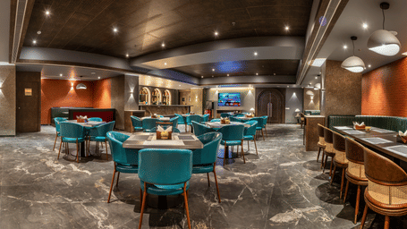The stylish interior of Distil Bar featuring plush teal and mustard seating, marble tables, and warm ambient lighting – Skkylight Lords Inn, Nanded