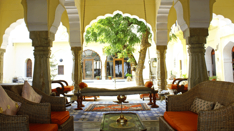 An inviting courtyard lounge at Fort Barli, with plush seating framed by arched columns, opens onto a lush garden view.