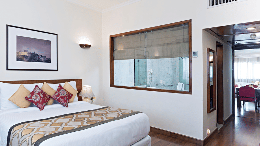 Presidential suite's bedroom with king-size bed, patterned cushions, wooden flooring and corridor view at Clarks Amer, Jaipur.