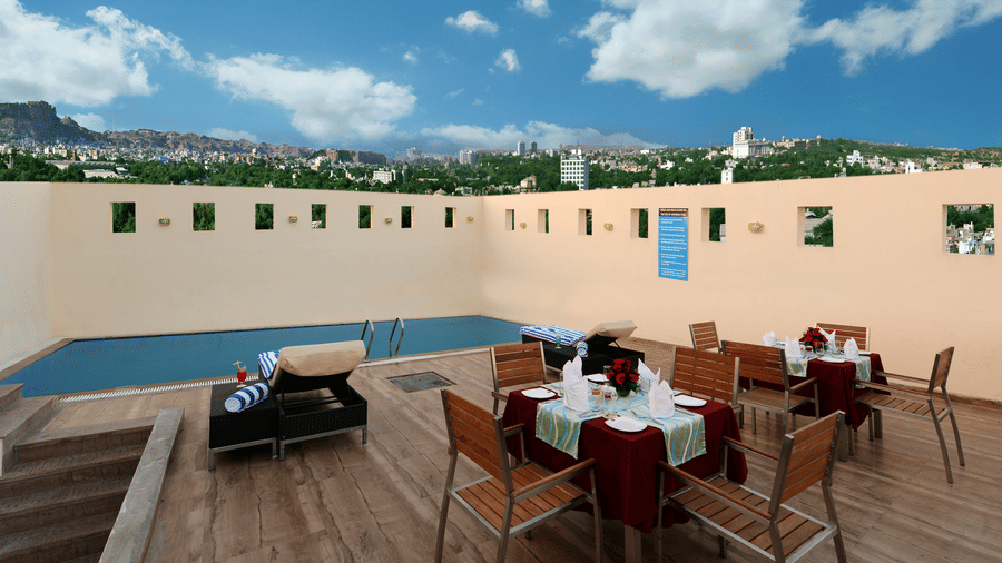 A side angle picture of a roof top pool with tables set for dinner, stairs and city lights view