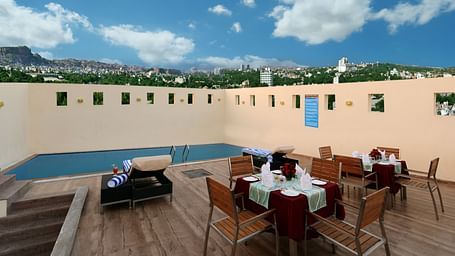 A side angle picture of a roof top pool with tables set for dinner, stairs and city lights view