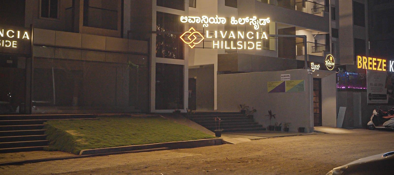 Closer view of the hotel entrance at night with illuminated signage and stairs leading up at TGI Livancia Hillside, JC Nagar, Mysore