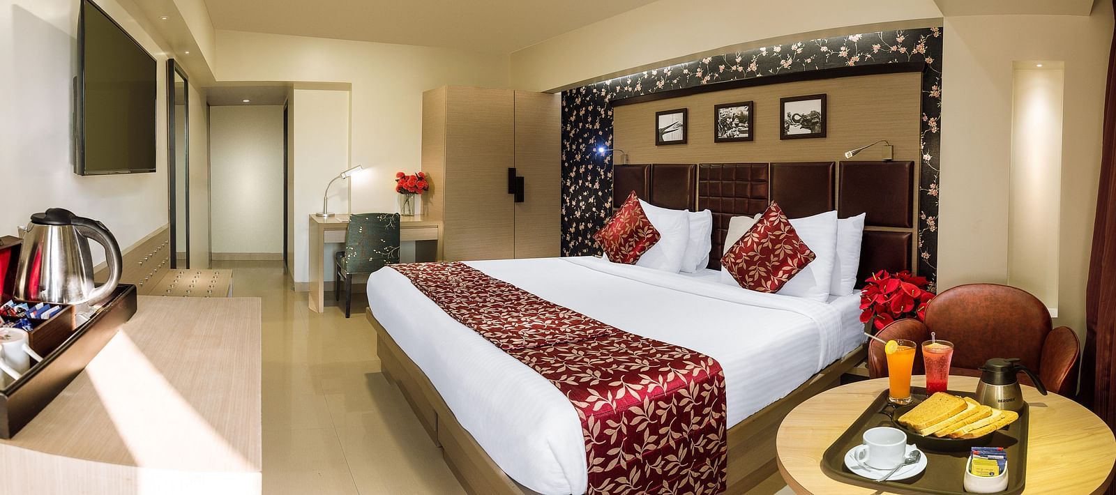 Spacious room with neatly made bed, a table with a food tray, and a wall-mounted TV opposite the bed at Oriental Aster, Mumbai.