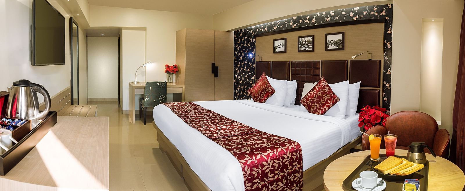 Spacious room with neatly made bed, a table with a food tray, and a wall-mounted TV opposite the bed at Oriental Aster, Mumbai.