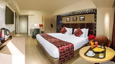 Spacious room with neatly made bed, a table with a food tray, and a wall-mounted TV opposite the bed at Oriental Aster, Mumbai.