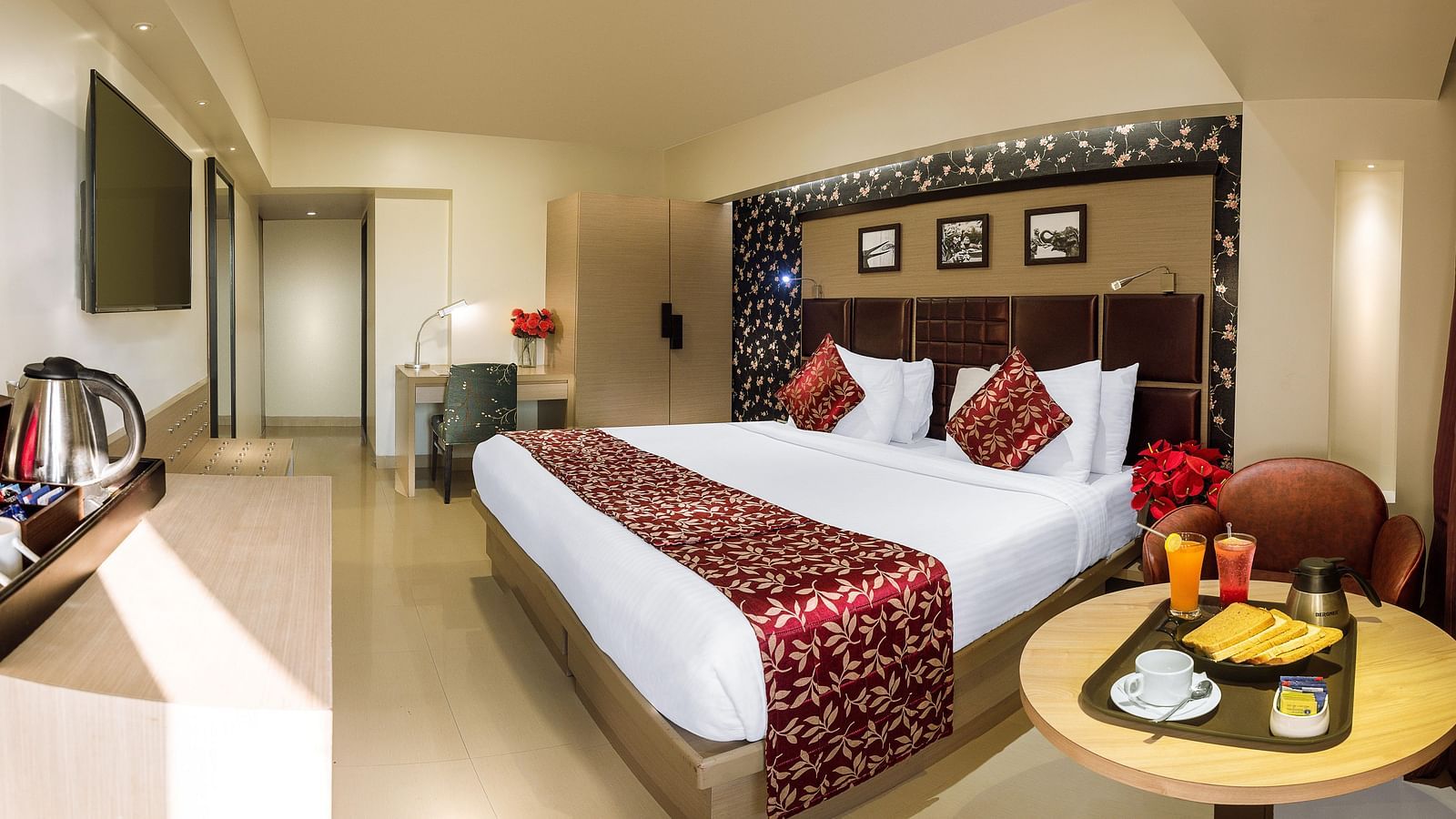 Spacious room with neatly made bed, a table with a food tray, and a wall-mounted TV opposite the bed at Oriental Aster, Mumbai.
