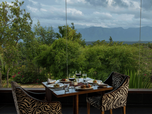 An outdoor dining area for two at The Sanctuary restaurant with a scenic view of the hills at The Serai Bandipur.