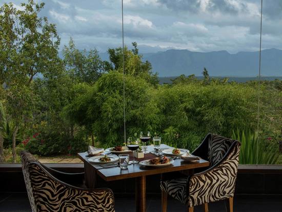 An outdoor dining area for two at The Sanctuary restaurant with a scenic view of the hills at The Serai Bandipur.