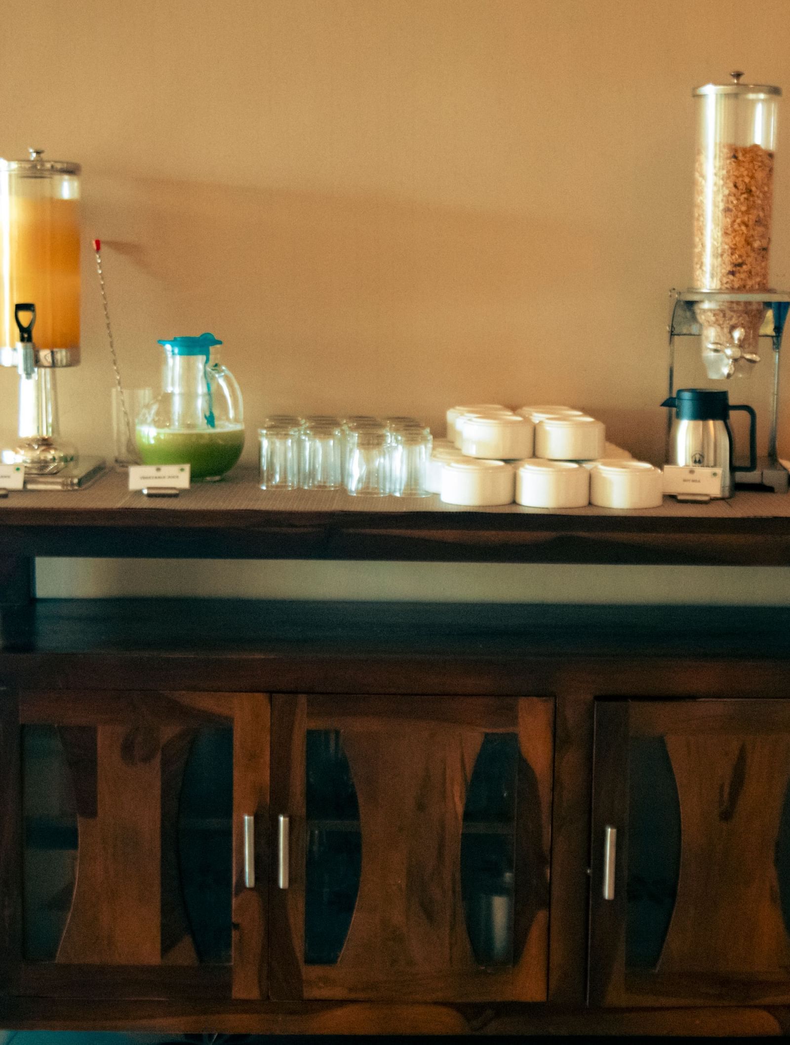 Beverage station with juice dispensers, cups, bowls, and a coffee machine placed on a wooden counter at Fireflies Resorts, Kabini.