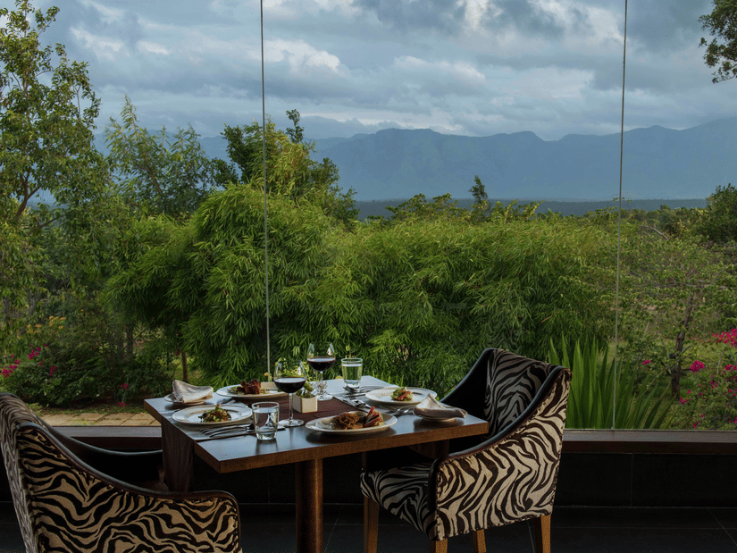 An outdoor dining area for two at The Sanctuary restaurant with a scenic view of the hills at The Serai Bandipur.