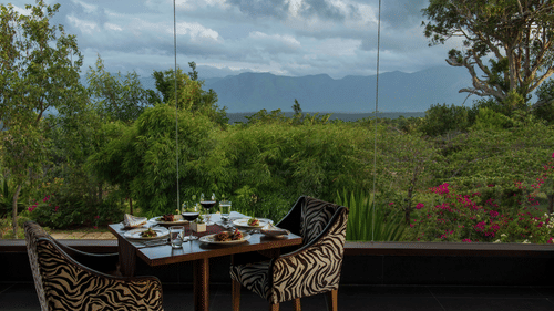 An outdoor dining area for two at The Sanctuary restaurant with a scenic view of the hills at The Serai Bandipur.
