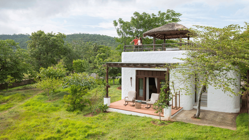 Facade of The Residence, one of the best Cottages in Bandipur, surrounded by greenery at The Serai, Bandipur featuring a couple on the terrace.