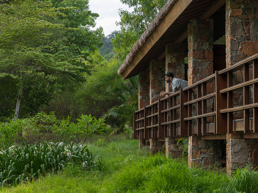 A person leaning out of balcony of Courtyard Superior Villas in Bandipur with greenery all around at The serai Bandipur