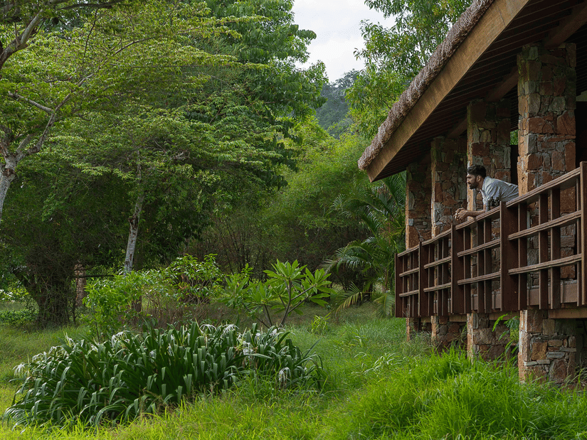 A person leaning out of balcony of Courtyard Superior Villas in Bandipur with greenery all around at The serai Bandipur