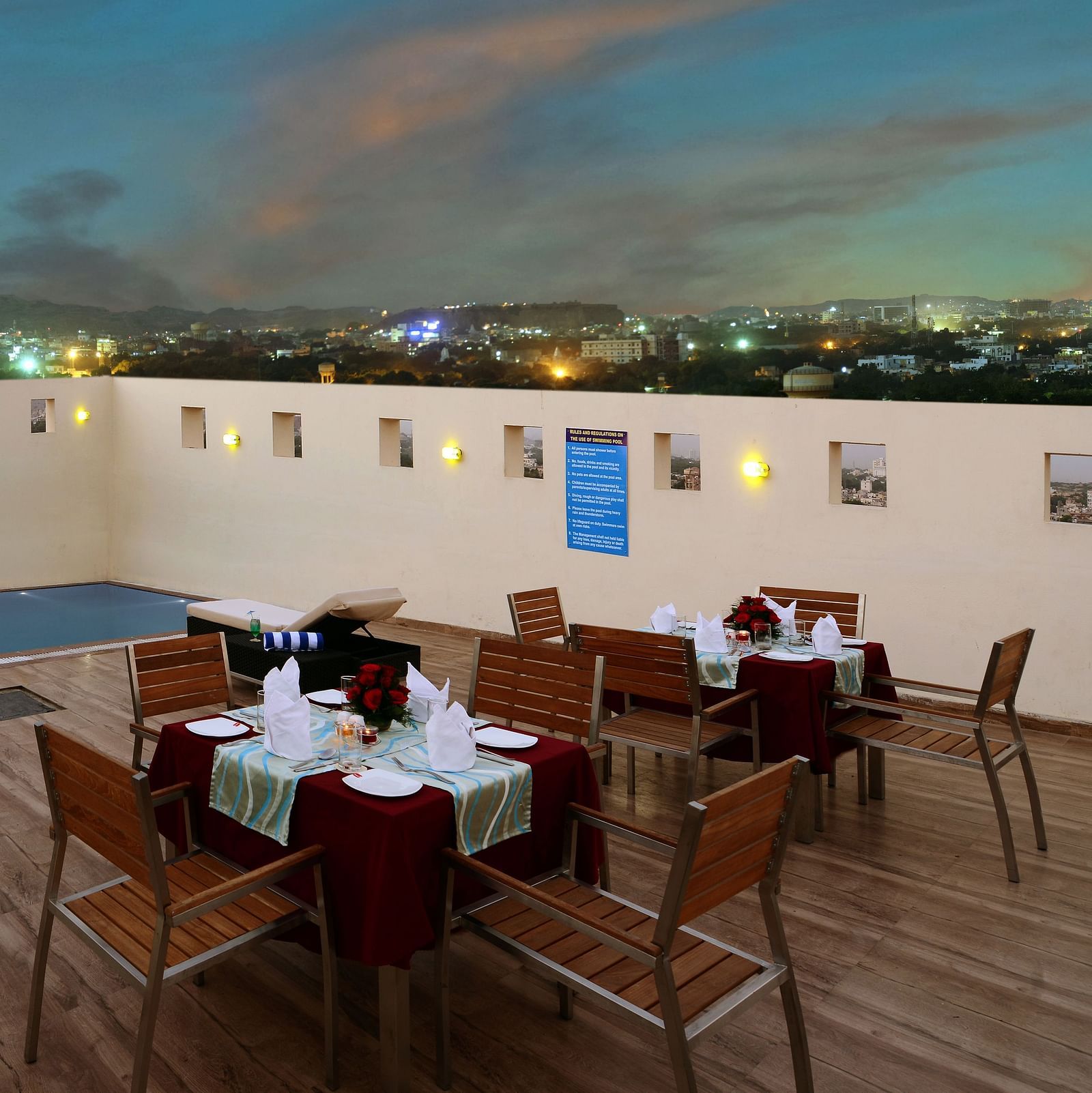 Rooftop pool with tables set for dinner and city lights view