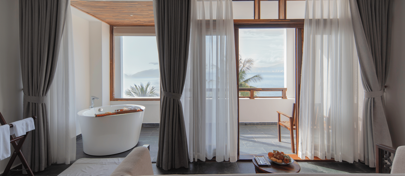 Executive Ocean Suite at Alibu Resort Nha Trang, Vietnam with bathtub, glass windows, seating area, open curtains and garden view bringing outside light.