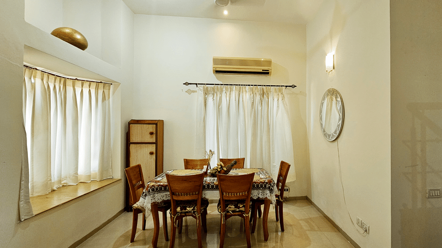 A cosy dining area surrounded with windows on 2 sides covered with curtains at Amara Villa, Nagoa.