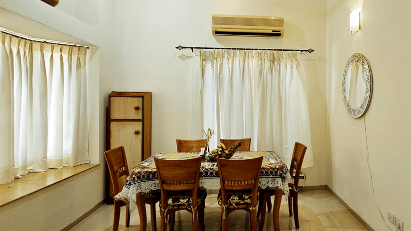 A cosy dining area surrounded with windows on 2 sides covered with curtains at Amara Villa, Nagoa.