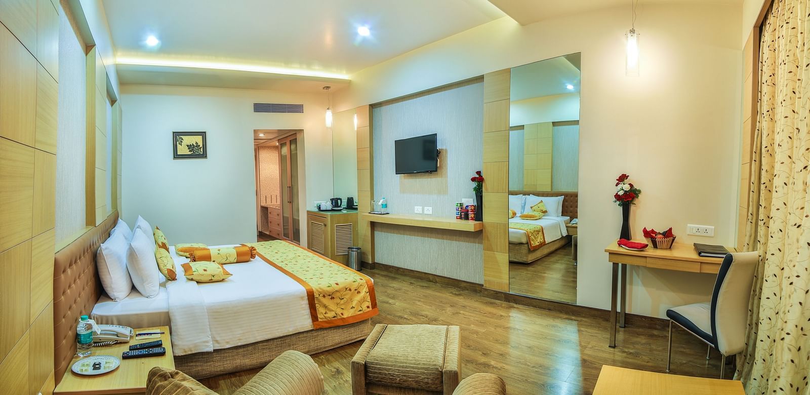 A king-sized hotel room with a contemporary design, a comfortable seating area, and a large television A grand hotel suite with an opulent red and white decor, large bed, and seating area, reflecting a traditional style at Sitara Luxury Hotel in Hyderabad 