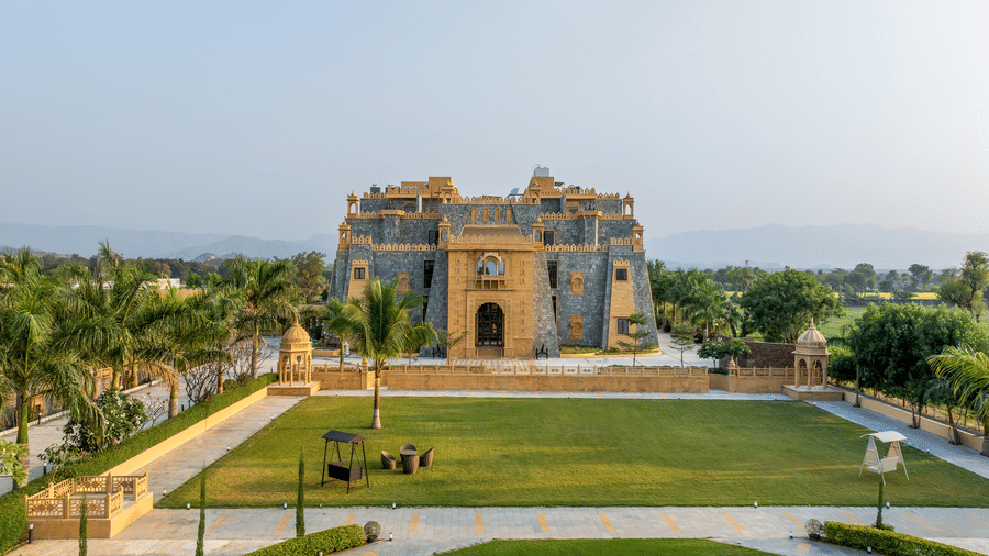 A view of the large green lawn in front of the primary stone structure at EsthereaRaj Leela, Ranakpur under a clear sky.