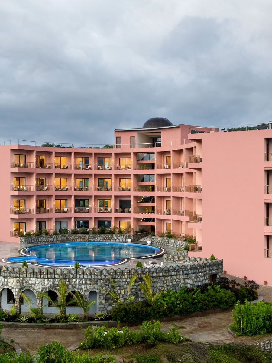 Facade of the Osian Valley Resort & Spa, a multi-story, pink-coloured structure with a large swimming pool in the foreground.