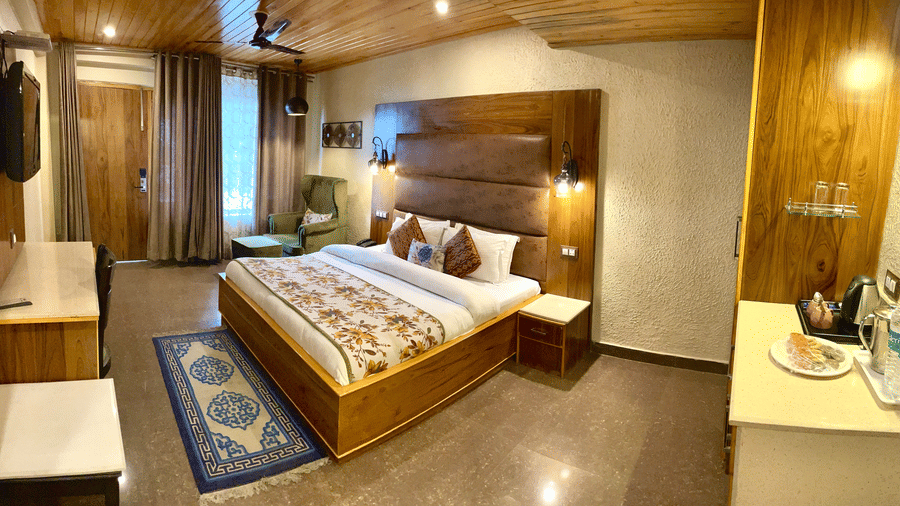 A neatly made bed and wooden furniture in a well-furnished Superior Room at Mongas Hotel & Resort, Dalhousie.
