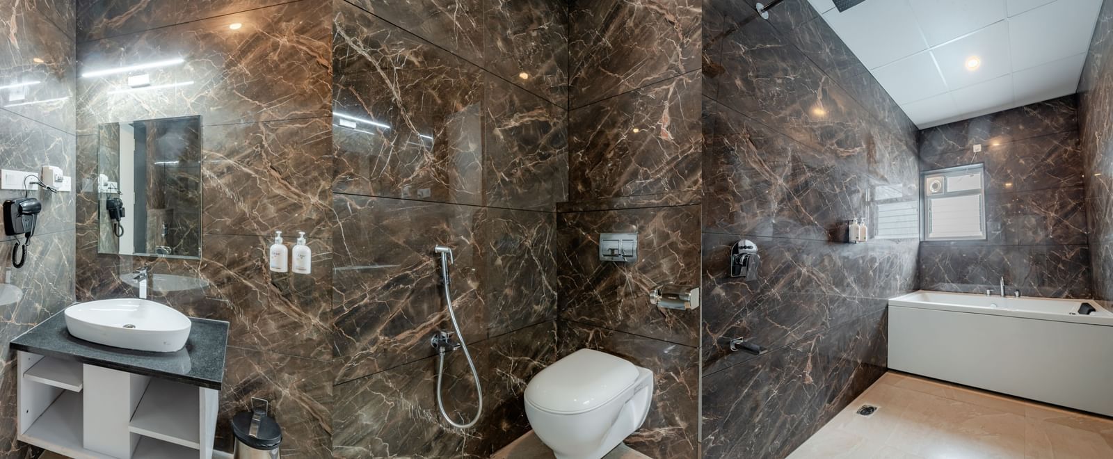Bathroom in the suite with dark marble-like tiles and a modern bathtub | Studio Suite | Pravasa Hotel, Vijayapura