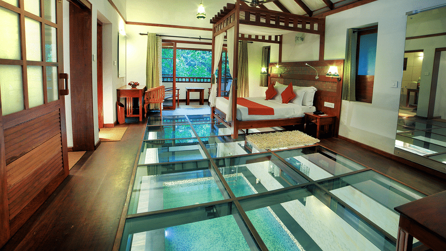 A side view of a glass-floored room with a bed and other wooden furnishings | Vythiri Resort. Wayanad