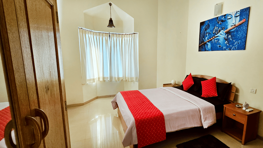 Side-view shot of a bedroom with a double bed in the middle along with a red-coloured bed runner and a wall-mounted art piece at Amara Villa, Nagoa.